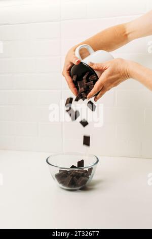 Les morceaux de chocolat noir sont versés dans une plaque de verre sur le dessus. Vue latérale. Banque D'Images