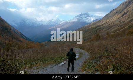 Randonneur touristique marchant sur un chemin de randonnée rocheux le long de montagnes géantes. Créatif. Homme solitaire marchant dans une gorge le long de l'herbe jaune. Banque D'Images