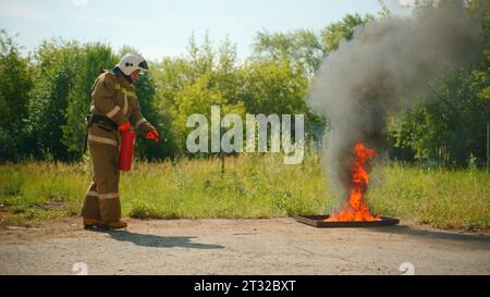 Pompier en casque et uniforme de protection éteignant le feu qui éclate de sous le sol. Clip. Concept de sauver des vies, héroïque Banque D'Images