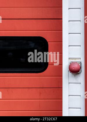 Partie d'une porte rouge et blanche de caserne de pompiers, gros plan du bouton d'ouverture et de la vitre teintée Banque D'Images