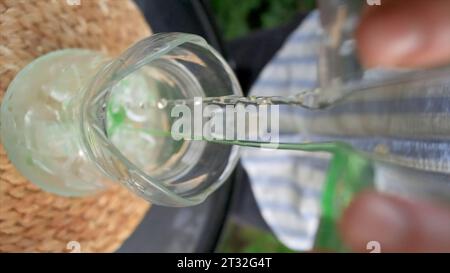 Une boisson rafraîchissante est versée sur la véranda d'été. Clip. Prise de vue verticale de jets éclairés de boissons dans des verres en verre. Verser une boisson fraîche avec Banque D'Images