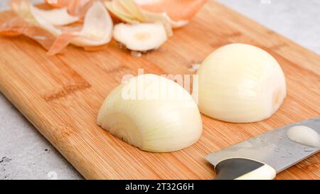 Éplucher et couper l'oignon blanc sur une planche à découper. Recette de soupe de légumes. Gros plan des ingrédients sur la table de cuisine Banque D'Images