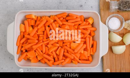 Recette de soupe de courge butternut rôtie. Gros plan des cubes de courge pelés et sans pépins, de la carotte, de l'oignon, de l'ail et des épices dans un plat en céramique sur le kit Banque D'Images