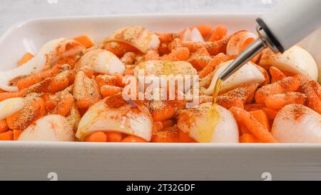 Recette de soupe de courge butternut rôtie. Gros plan des cubes de courge pelés et sans pépins, de la carotte, de l'oignon, de l'ail et des épices dans un plat allant au four en céramique, garniture W. Banque D'Images