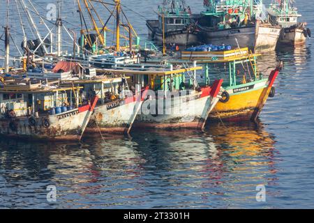 Bateaux de pêche commerciaux ancrés dans des eaux calmes au coucher du soleil avec des reflets colorés dans l'eau Banque D'Images