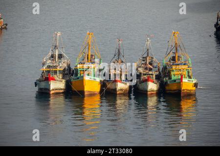 Bateaux de pêche commerciaux ancrés dans des eaux calmes au coucher du soleil avec des reflets colorés dans l'eau Banque D'Images