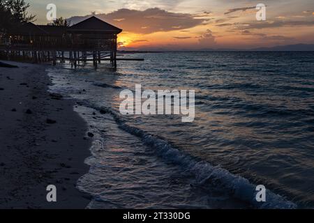 Lever du soleil à quai et gazebo sur une plage tropicale et vagues douces roulent Banque D'Images