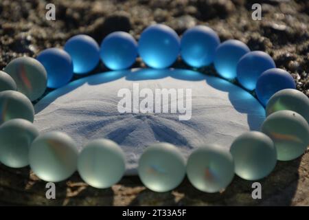 Art original par moi. Dollar de sable blanc avec des billes de verre de mer claires et bleues. Banque D'Images