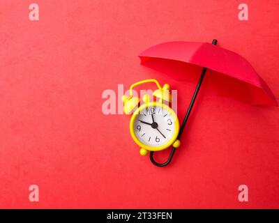 Un réveil jaune avec parapluie rouge sur fond rouge avec espace de copie. Banque D'Images