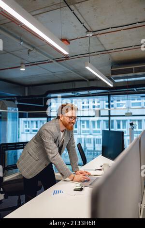 Souriant homme pdg travaillant sur un ordinateur portable debout près du bureau dans un bureau moderne Banque D'Images