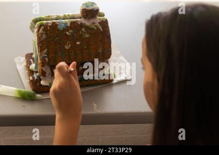 maison en pain d'épice. Petite fille dans les préparations de vacances mettant le vitrage sur la maison de pain d'épice arbres de Noël. Banque D'Images