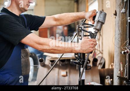 Vue rognée de travailleur professionnel, réparateur, mécanicien travaillant dans le garage, atelier. Homme tenant, utilisant l'équipement, l'instrument. Concept de travail manuel. Banque D'Images