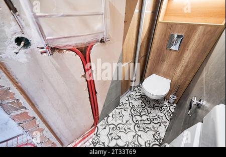 Comparaison des toilettes avant et après rénovation. Ancien appartement toilettes avec tuyaux de chauffage au sol et nouvelle salle de toilette rénovée avec sèche-serviettes électrique. Banque D'Images
