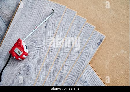 Ruban de mesure sur des planches de parquet pour la rénovation de la maison, les travaux de construction et la décoration intérieure. Mètre à ruban sur des échantillons de panneaux stratifiés avec motif et texture du bois pour le revêtement de sol. Banque D'Images
