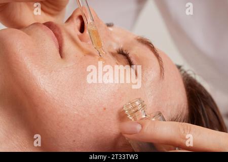 Gros plan du processus d'une esthéticienne appliquant de l'huile sur le visage d'une femme avec une pipette soins de la peau faciaux avec de l'huile cosmétique médicamenteuse. tenez-vous professionnel Banque D'Images