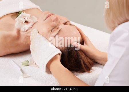 Les mains de l'esthéticienne essuyez le visage de la jeune fille dans le centre de cosmétologie avec des gants blancs.Portrait d'une belle fille sur la procédure pour rajeunati Banque D'Images