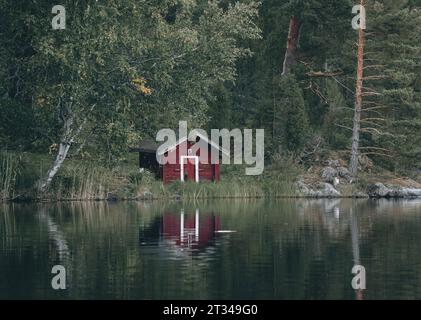 Petite maison en bois rouge au bord d'un lac en Finlande Banque D'Images
