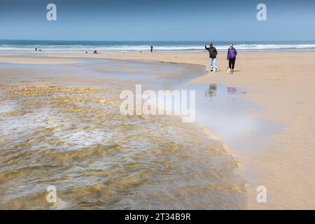 Les gens qui marchent le long de la rivière Menalhyl qui traverse la plage à Mawgan Porth, dans les Cornouailles, au Royaume-Uni. Banque D'Images