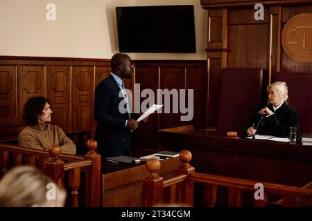 Avocat jeune homme confiant avec le document regardant le juge femme mature pendant la consultation ou l'appel sur l'affaire de la cour pendant la session de procès Banque D'Images