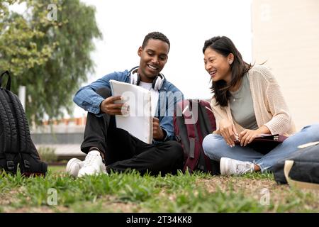 Divers couple d'étudiants assis à l'extérieur lisant des documents.deux jeunes étudiants multiraciaux regardant des notes assis sur le campus d'étage. Banque D'Images