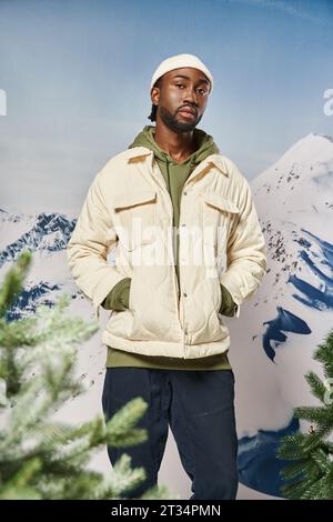 bel homme en veste blanche et bonnet beanie posant avec les mains dans les poches, la mode et le style Banque D'Images