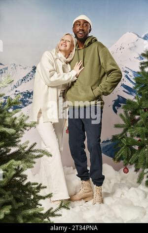 femme blonde joyeuse serrant avec petit ami afro-américain avec toile de fond de montagne, mode d'hiver Banque D'Images