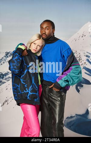 beau jeune couple dans des tenues chaudes serrant amoureusement avec toile de fond de montagne, concept d'hiver Banque D'Images