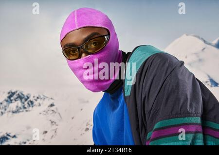bel homme élégant portant balaclava rose et lunettes de soleil avec toile de fond enneigée, concept d'hiver Banque D'Images