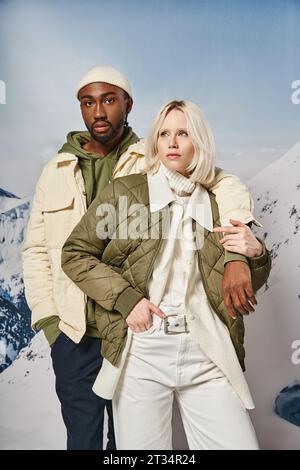 couple élégant attrayant dans des tenues de saison posant ensemble avec fond de montagne, concept d'hiver Banque D'Images