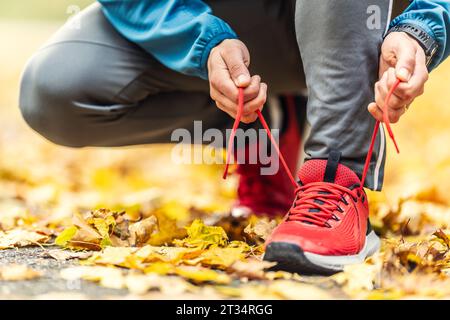 Vue rapprochée des mains d'un athlète nouant ses lacets avant de courir dans un parc d'automne. Banque D'Images