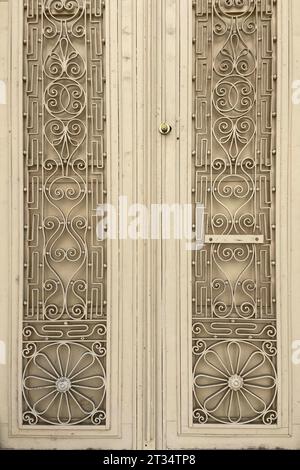Métal vieux beige double ailé lourd grande porte âgée avec ornements décoratifs en fer forgé, photo en gros plan de portes fermées d'une vieille maison Banque D'Images