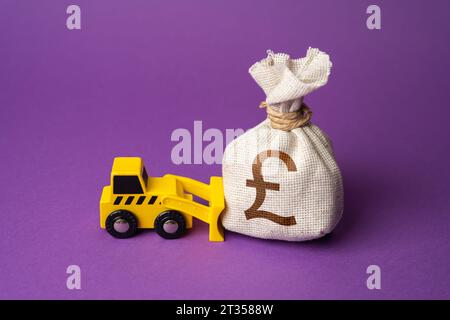 Un bulldozer pousse un sac de livres sterling. Utilisation inefficace des fonds. De l'argent dans les égouts. Financement des travaux de démantèlement. Démolition. IND Banque D'Images