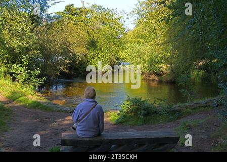 Femme assise seule sur un banc à côté de la rivière. Lumière du soir. Vue de l'autre côté de la rivière Ness près du centre d'Inverness. Inverness City, Highlands, Écosse, Royaume-Uni Banque D'Images