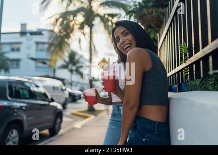 USA, Florida, Miami Beach, deux joyeux amis féminins ayant une boisson gazeuse dans la ville Banque D'Images