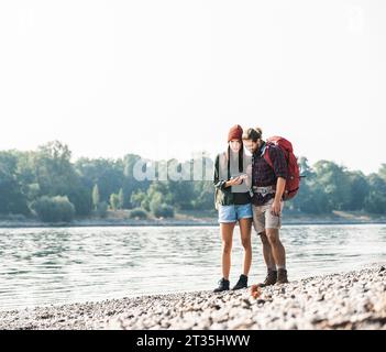 Jeune couple avec des sacs du riverside contrôle cell phone Banque D'Images