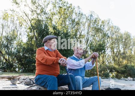 Deux vieux amis assis sur un tronc d'arbre par le partage de souvenirs, riverside Banque D'Images