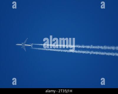 Télé gros plan d'un avion de ligne volant à haute altitude avec des contrails dans un ciel bleu clair Banque D'Images