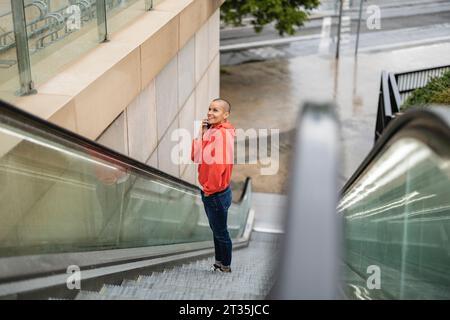 Femme parlant à travers le téléphone intelligent et se déplaçant vers le haut sur l'escalator Banque D'Images