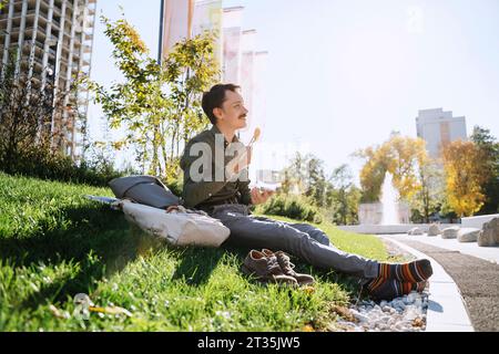 Homme d'affaires prenant le déjeuner assis sur l'herbe au parc de bureau Banque D'Images