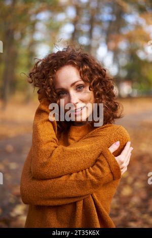 Femme rousse souriante portant un pull au parc d'automne Banque D'Images