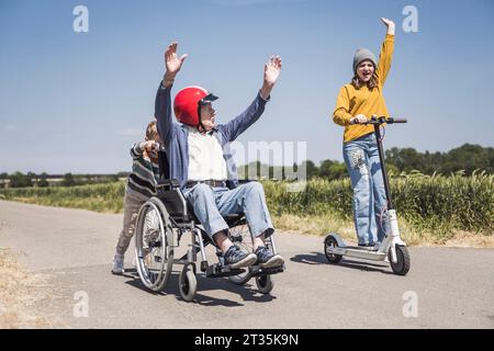 Fille debout sur scooter de poussée électrique avec grand-père assis en fauteuil roulant Banque D'Images