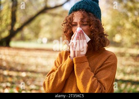 Redhead femme soufflant le nez avec du tissu facial au parc d'automne Banque D'Images