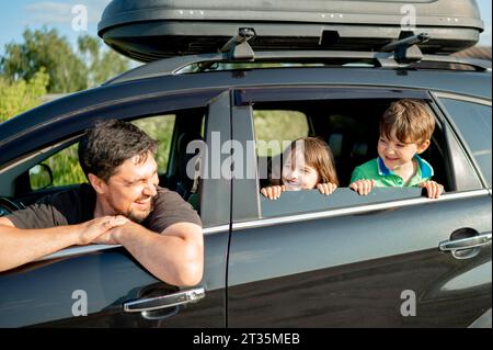 Père heureux avec des enfants regardant par la fenêtre de la voiture le jour ensoleillé Banque D'Images