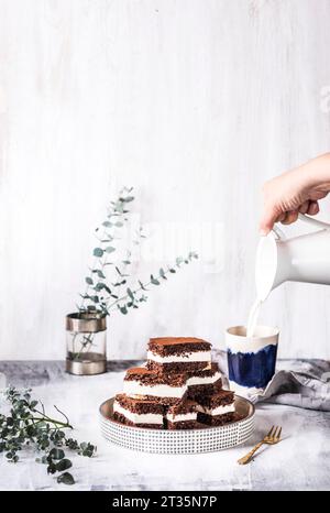 Main de femme versant le lait dans la tasse avec gâteau au chocolat sur la table Banque D'Images