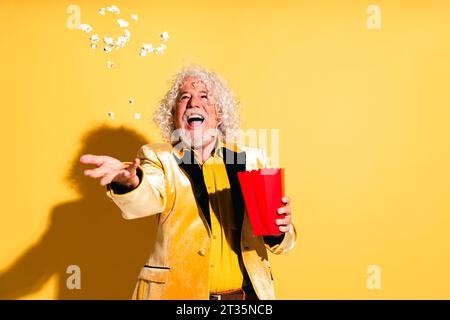 Homme senior joyeux attrapant pop-corn sur fond jaune Banque D'Images