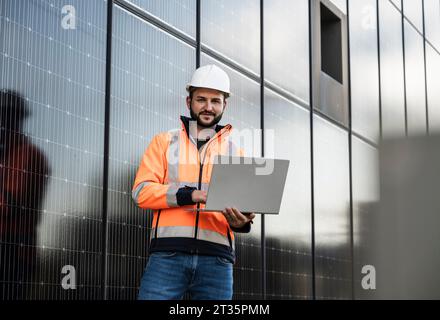 Ingénieur souriant tenant un ordinateur portable debout près des panneaux solaires Banque D'Images