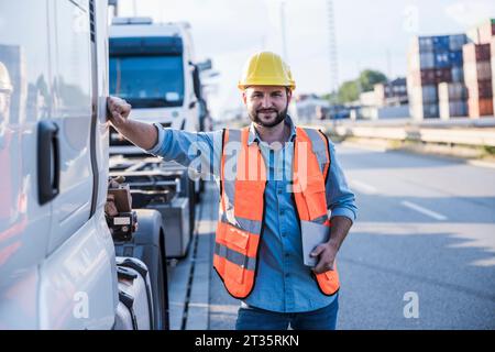 Chauffeur de camion souriant portant un casque dur debout avec tablette PC par camion Banque D'Images