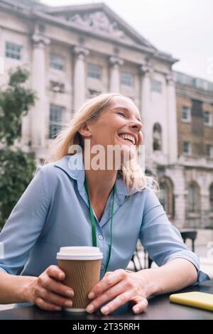Joyeuse femme d'affaires riant avec tasse jetable au café Banque D'Images