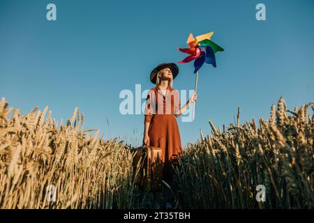 Femme tenant la valise debout avec le jouet Pinwheel dans le champ de blé Banque D'Images