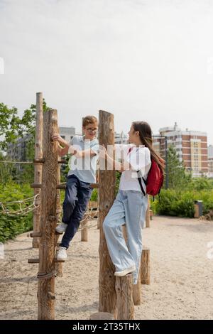 Amis grimpant sur un poteau en bois à l'aire de jeux Banque D'Images